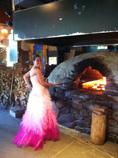 Woman in prom dress baking a pizza in a clay oven