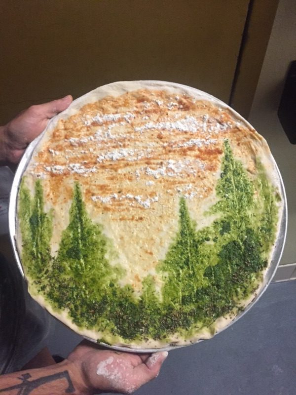 Image of a pizza with a forest scene made from pesto