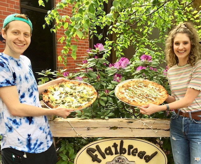 people with pizza in front of flatbread sign
